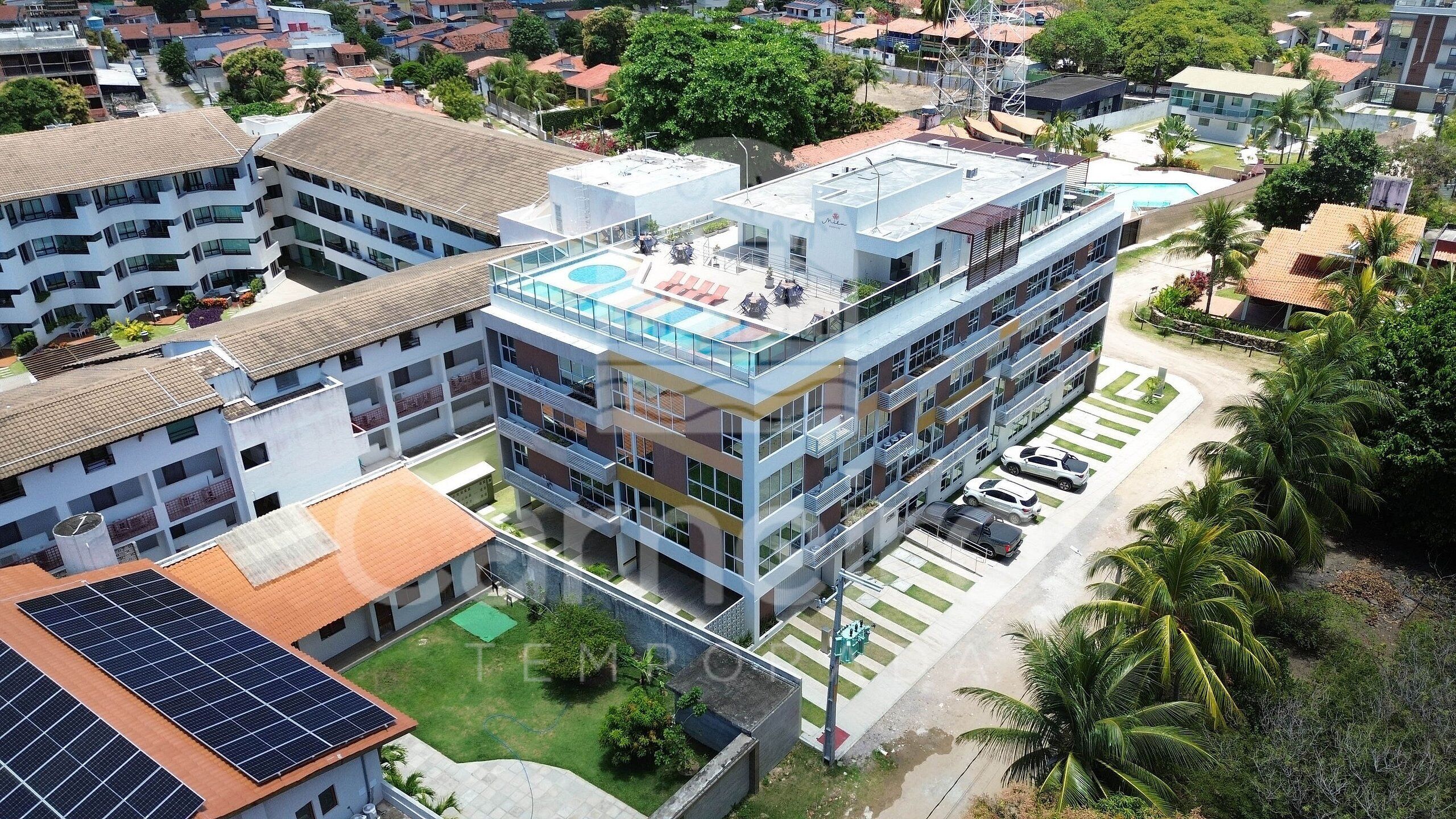 A multi-story building with a rooftop pool, solar panels, and a parking area.