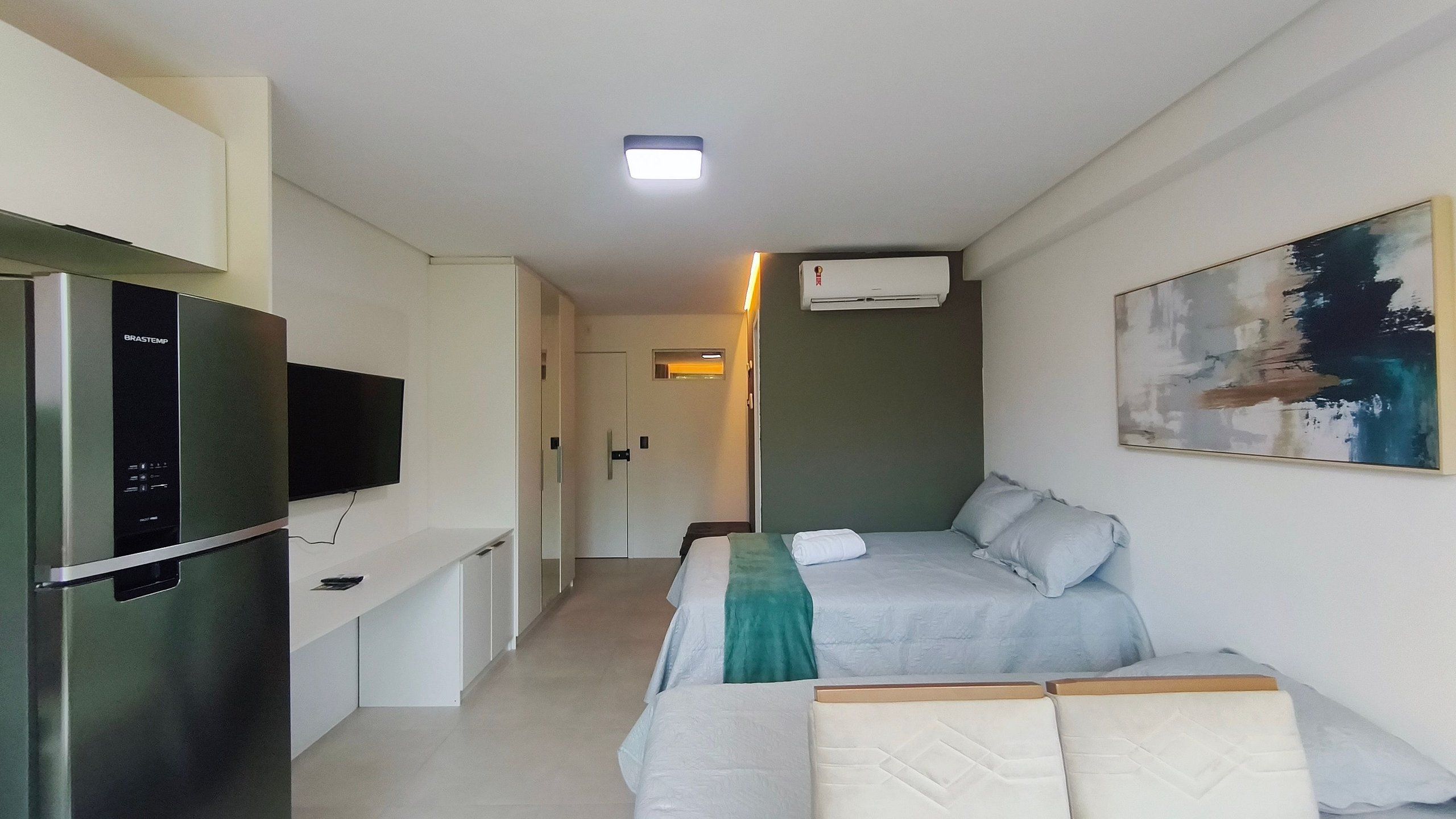 Quarto de hotel pequeno com uma cama, televisão, frigorífico e ar condicionado.