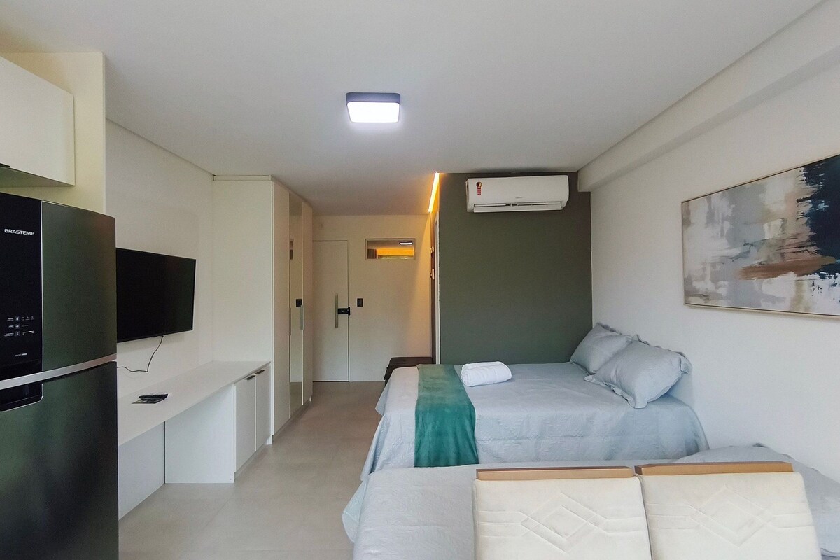 Ein kleines Hotelzimmer mit Bett, Fernseher, Kühlschrank und Klimaanlage.