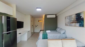 Ein kleines Hotelzimmer mit Bett, Fernseher, Kühlschrank und Klimaanlage.