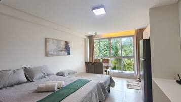 A hotel room with a bed, a desk, a chair, a television, and a window with a view of greenery.