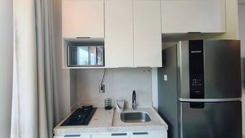 A compact kitchen with a stainless steel refrigerator, a built-in oven, and a small window above the oven.