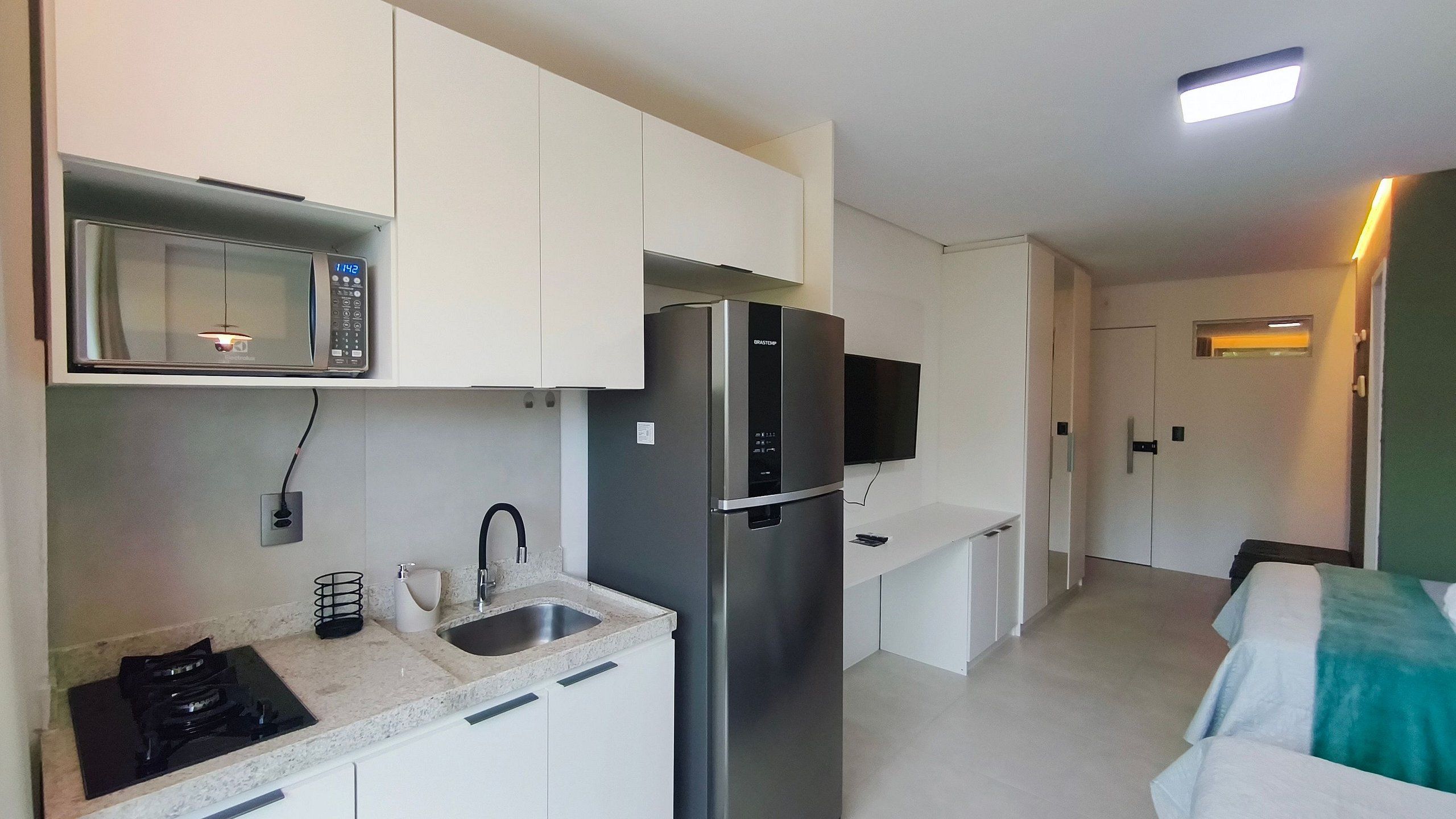 Eine moderne Küche mit Mikrowelle, Kühlschrank, Spüle und einem Flachbildfernseher.
