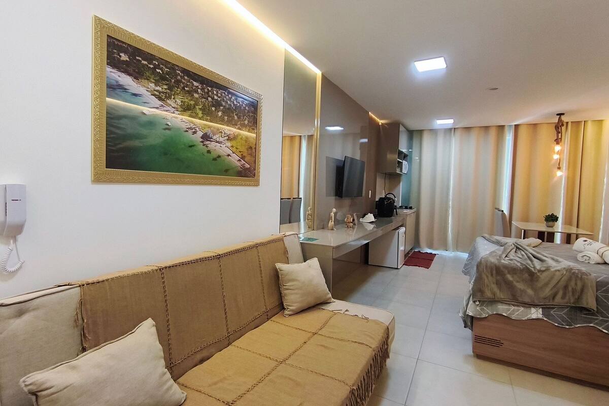 A hotel room with a sofa, a bed, a desk, a TV, and a painting on the wall.