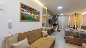 A hotel room with a sofa, a bed, a desk, a TV, and a painting on the wall.