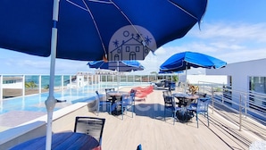 A poolside area with umbrellas, lounge chairs, and a view of the ocean. - Mila Rooftop - Praia de Tamandaré (Tamandaré)