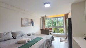 A hotel room with a bed, a desk, a chair, a television, and a window with a view of greenery. - Mila Rooftop - Praia de Tamandaré (Tamandaré)
