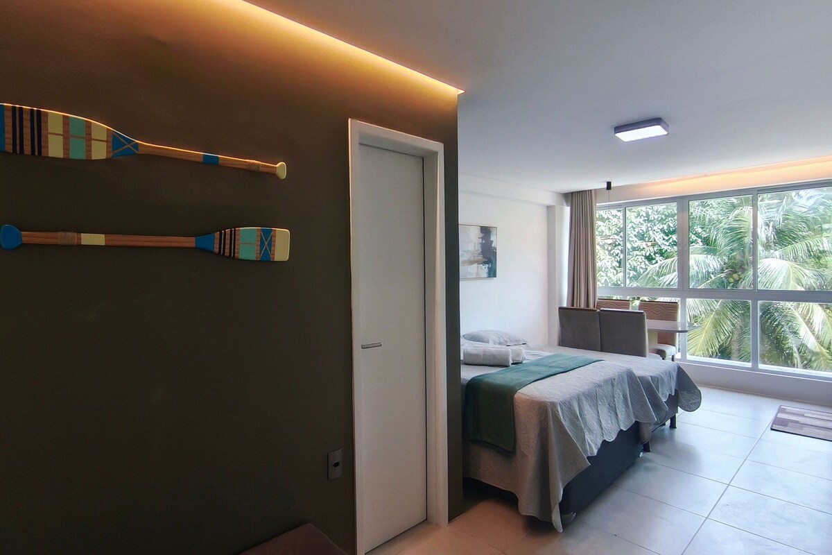 A hotel room with a bed, a bathroom, and a view of palm trees.