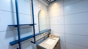 Un baño con pared de azulejos blancos, un espejo, un lavabo con encimera de granito y un perchero azul.