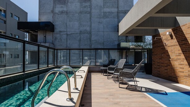 A rooftop pool area with a glass balustrade, lounge chairs, and a view of the cityscape.