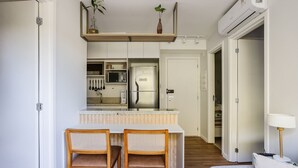 A modern kitchen with a built-in microwave, refrigerator, and a wooden shelf above the counter. There are two wicker chairs at a small dining table.