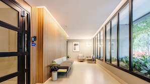 A modern hallway with a wooden slat wall, a seating area with a sofa and chairs, and large windows offering a view of greenery.