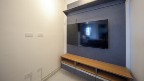 A modern living room with a flat-screen TV mounted on a grey wall, wooden entertainment unit below, and white walls.