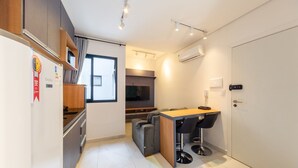 A compact kitchen with a built-in oven, a dining area with two stools, and a grey sofa.