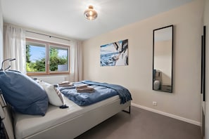 A bedroom with a bed, a window, a painting, and a mirror.