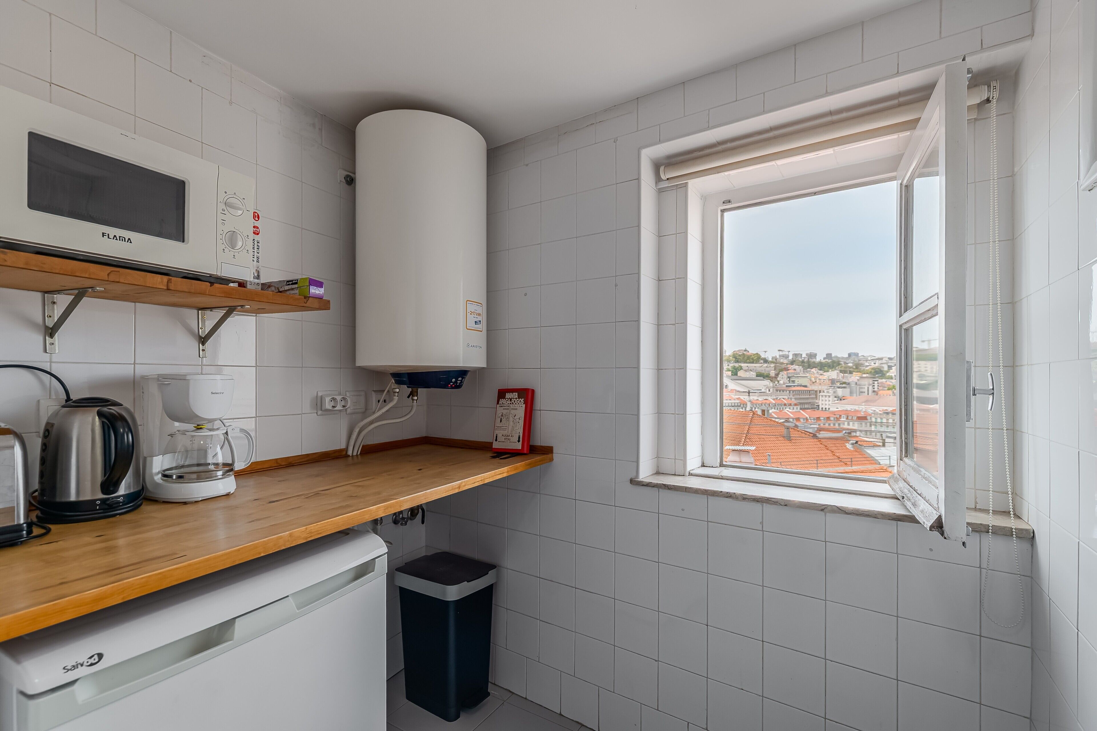Una cuina moderna amb microones, cafetera i vista a la ciutat a través d'una finestra.