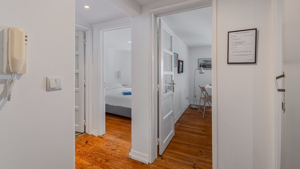 A hotel room with a wooden floor, a bed, a desk with a chair, and a wall-mounted phone.