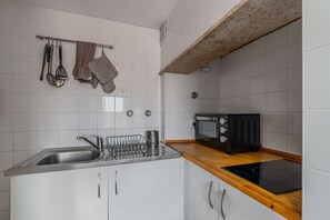 A kitchen with a stainless steel sink, a dish rack, a microwave, and an induction cooktop.