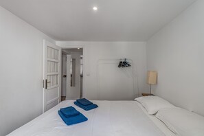 A bedroom with a bed, white walls, a door, a lamp, and a coat rack.
