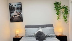Ein ordentlich eingerichtetes Schlafzimmer mit einem Bett, zwei Nachttischen, einer Wandpflanze und einem gerahmten Bild.