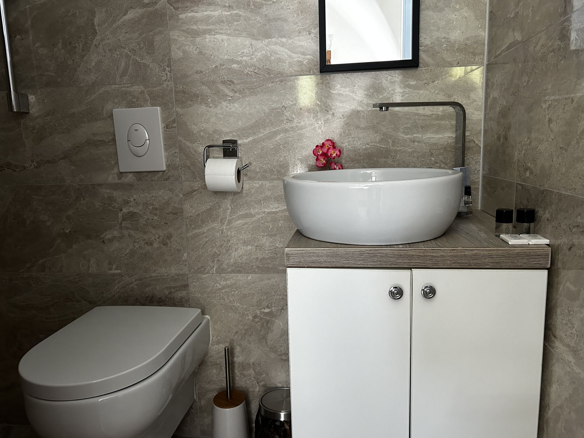 A modern bathroom with a toilet, a sink with a marble basin, and a cabinet with two drawers.