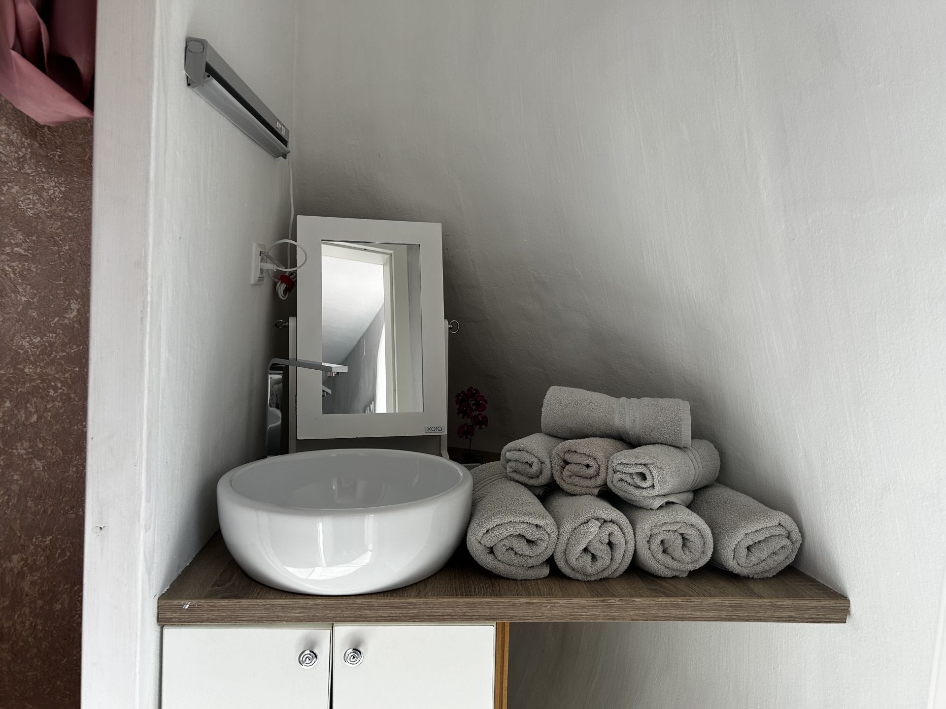 A bathroom with a white sink, a mirror, and a wooden shelf holding rolled towels.