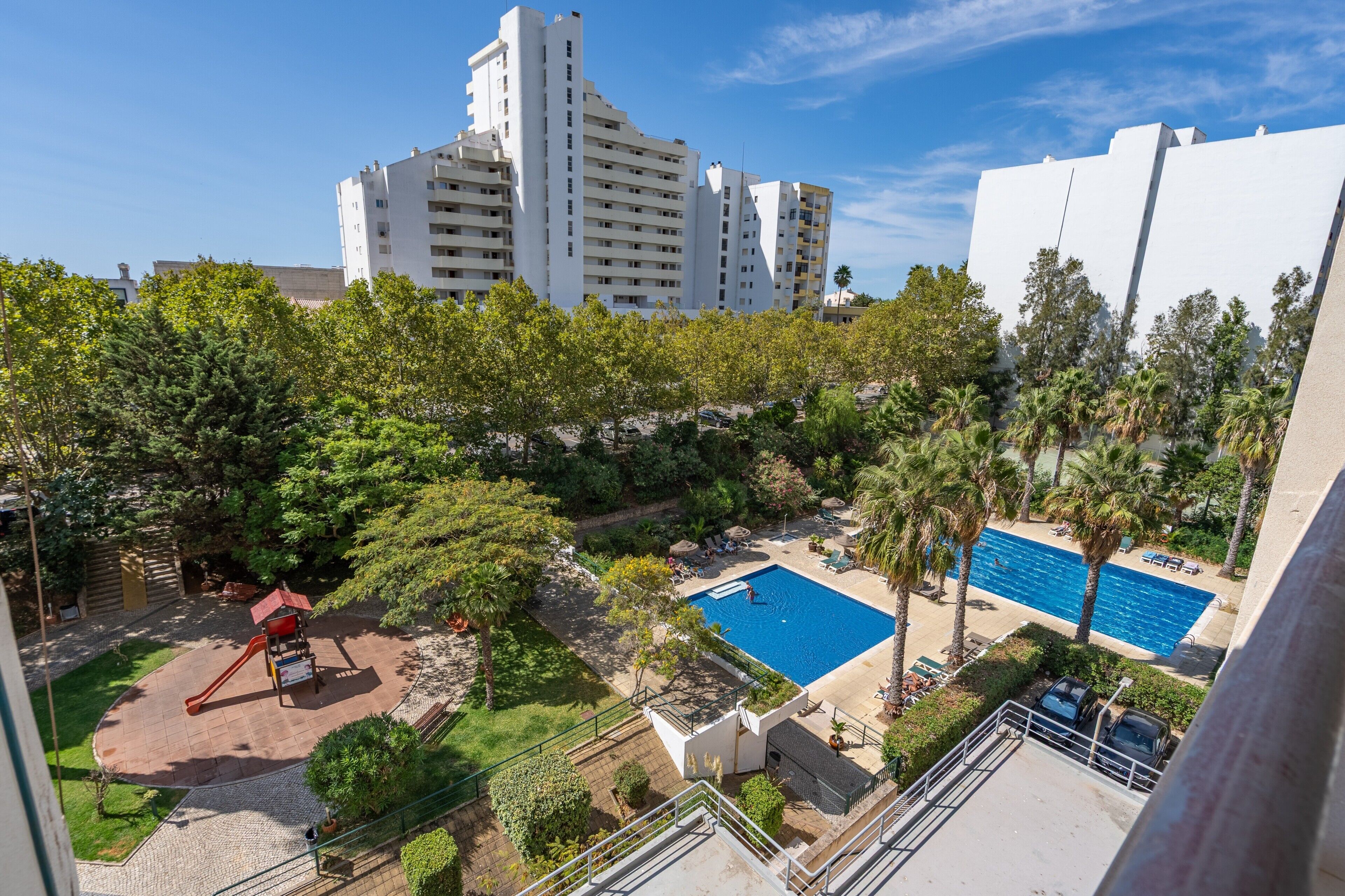 Área residencial com piscina, parquinho e edifícios altos ao fundo.
