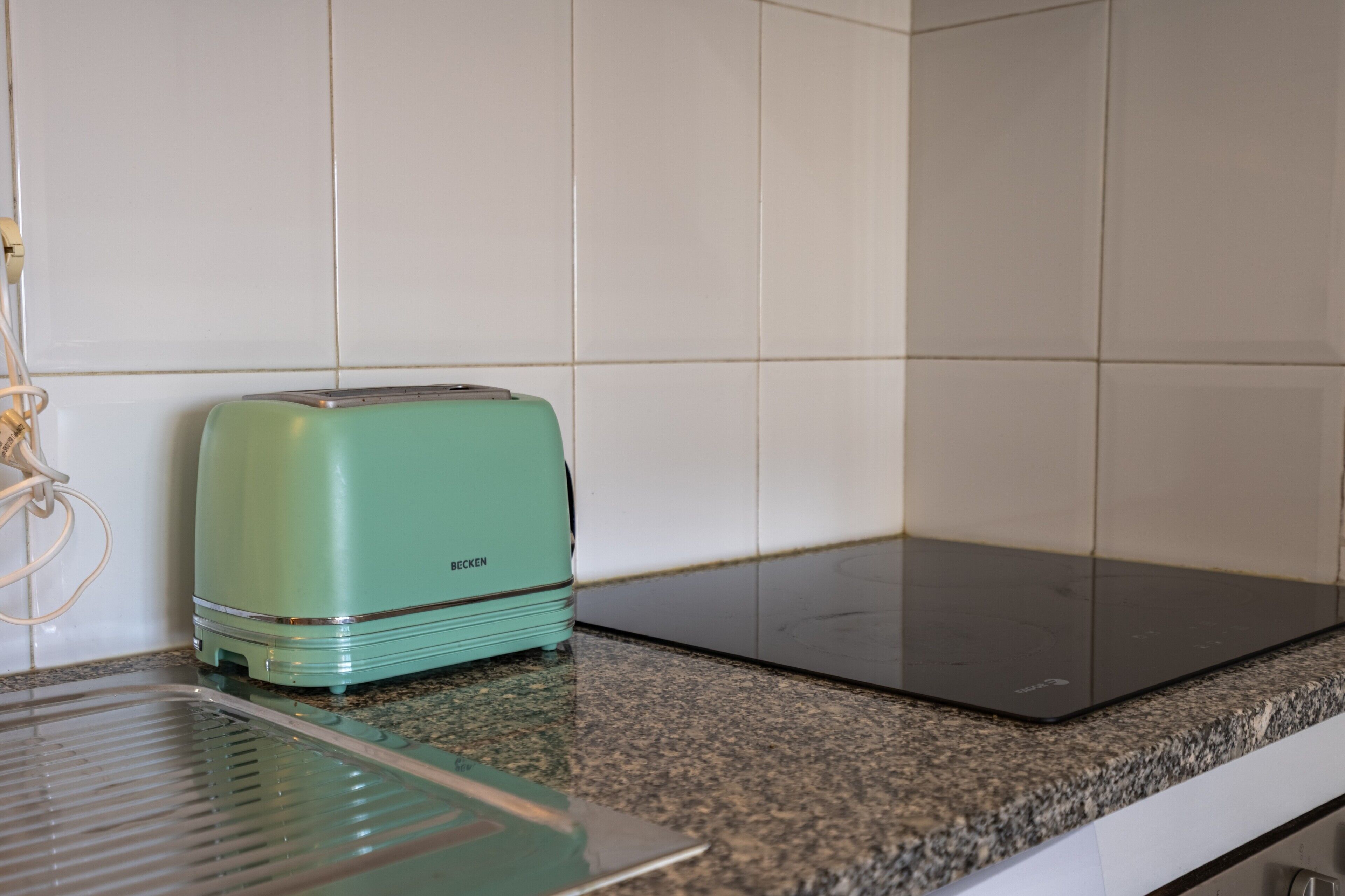 A kitchen with a green toaster, a black induction cooktop, and a granite countertop.
