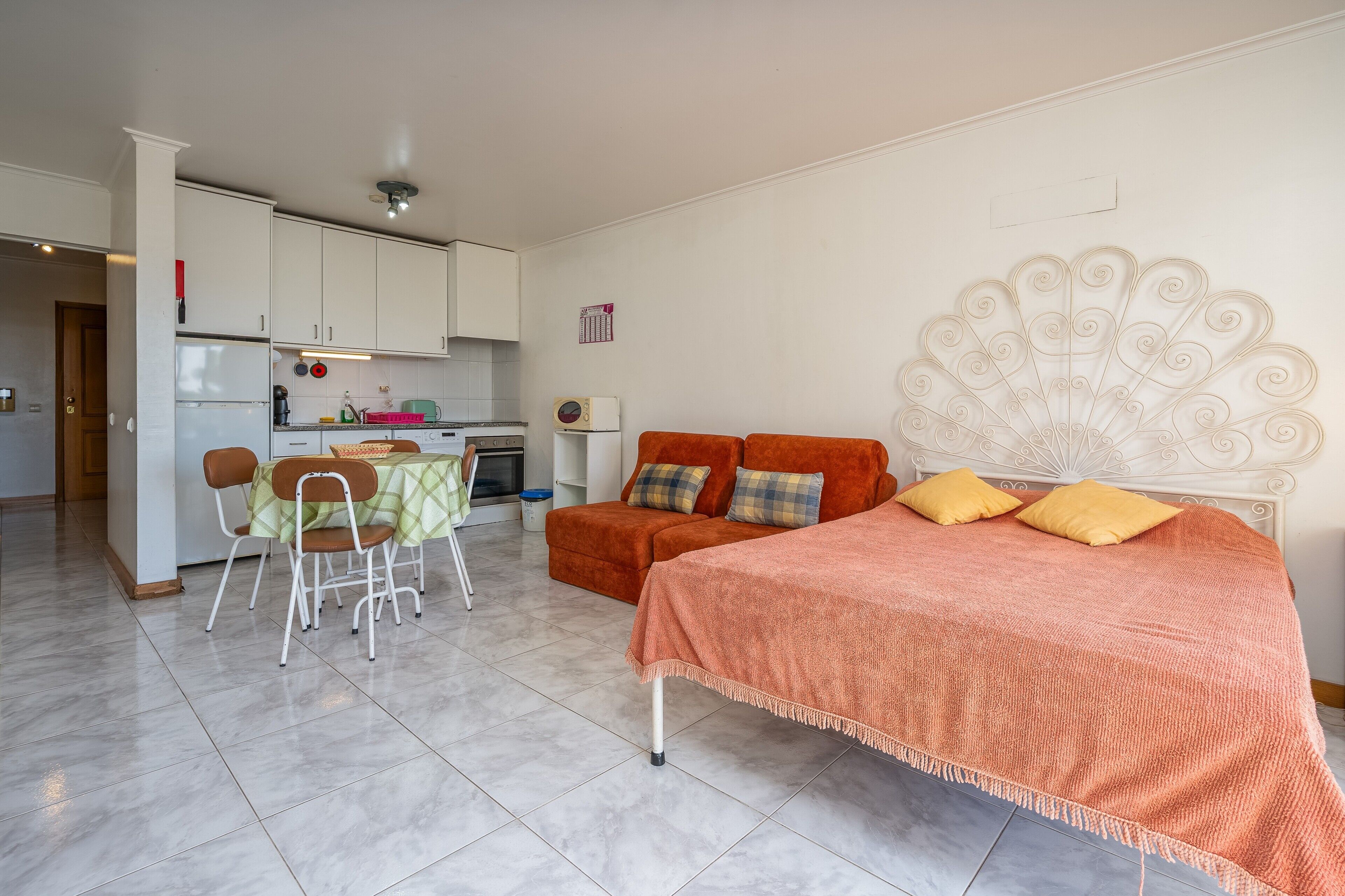 A compact room with a bed, a sofa, a dining table, and a kitchenette.