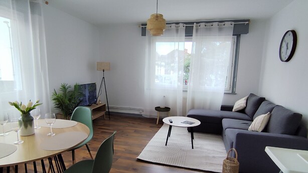 Un salon moderne avec une table de salle à manger ronde, des chaises vertes, un canapé gris et une petite table d’appoint.