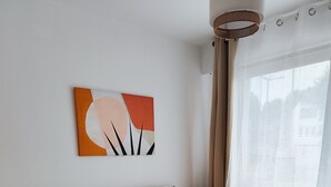 Une chambre à coucher avec un lit, une petite table de chevet ornée d’une plante et un tableau abstrait accroché au mur.