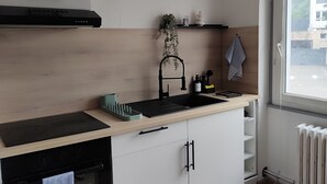 Une cuisine moderne dotée d’un four encastré, d’une plaque de cuisson noire, d’un plan de travail en bois, d’un évier noir et d’un luminaire suspendu.