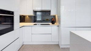A modern kitchen with white cabinetry, a built-in oven, and a central island with a sink.