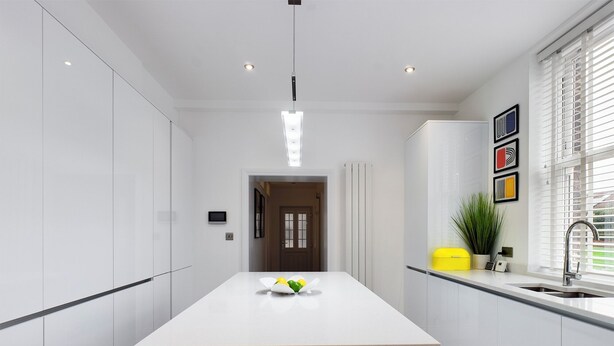 A modern kitchen with white cabinetry, a central island, a built-in sink, and a window with blinds.