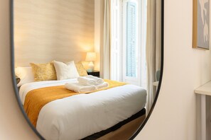Una habitación de hotel con una cama, una mesita de noche, una lámpara y una ventana.
