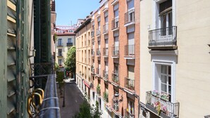 Une rue étroite bordée d’immeubles à plusieurs étages, avec des balcons dotés de garde-corps et de plantes en pot.