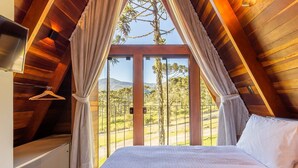 A bedroom with a large window, wooden ceiling beams, and a bed with white bedding. - RJF - Comfortable Chalets in Urubici (Urubici)