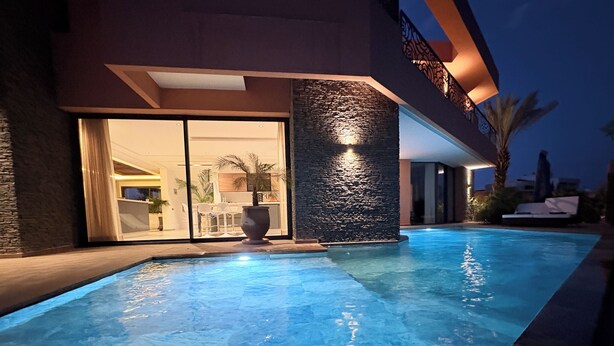 A swimming pool with a stone wall and a glass door leading to an indoor area. - New 480 m² villa with service 10 mn from center (Marrakech)