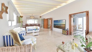 Un salón amplio con techo alto, un televisor de pantalla plana grande y un comedor con muebles de madera.