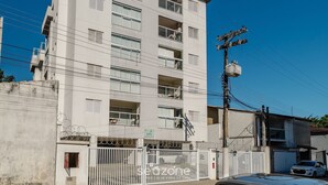 Un edificio de varios pisos con balcones, una entrada protegida por una reja y líneas eléctricas a la vista.