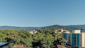 Zona residencial con edificios y árboles, cielo despejado y montañas al fondo.