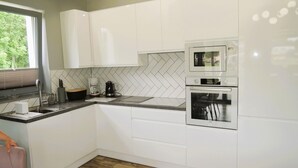 A modern kitchen with white cabinets, a herringbone tile backsplash, a built-in oven, and a microwave. - New, large holiday home for 10 people (Kołczewo)
