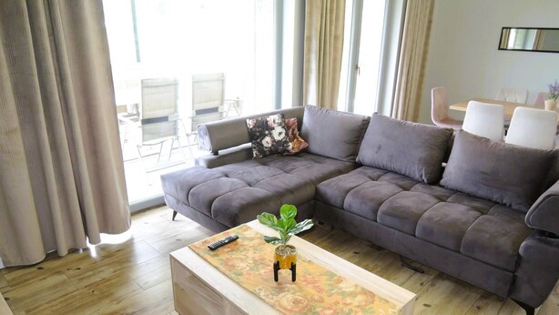 A modern living room with a sectional sofa, a wooden coffee table, and a dining area in the background. - New, large holiday home for 10 people (Kołczewo)
