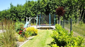 A fenced outdoor area with a trampoline, a slide, and various plants. - New, large holiday home for 10 people (Kołczewo)