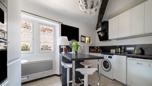 Une cuisine moderne équipée d’un lave-linge, d’un coin repas avec des tabourets de bar et d’une grande fenêtre agrémentée de plantes en pot.