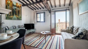 Un salon confortable avec un canapé, un téléviseur, une table à manger avec des chaises, un tapis coloré et un balcon doté d’une rambarde.