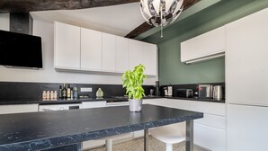 Une cuisine moderne avec des meubles blancs, un plan de travail noir, une plante en pot et une bouilloire en acier inoxydable.