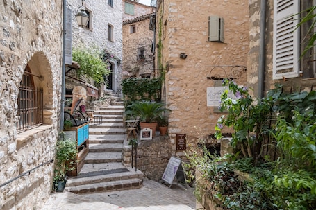 A narrow alley with stone buildings, a staircase, and potted plants.
