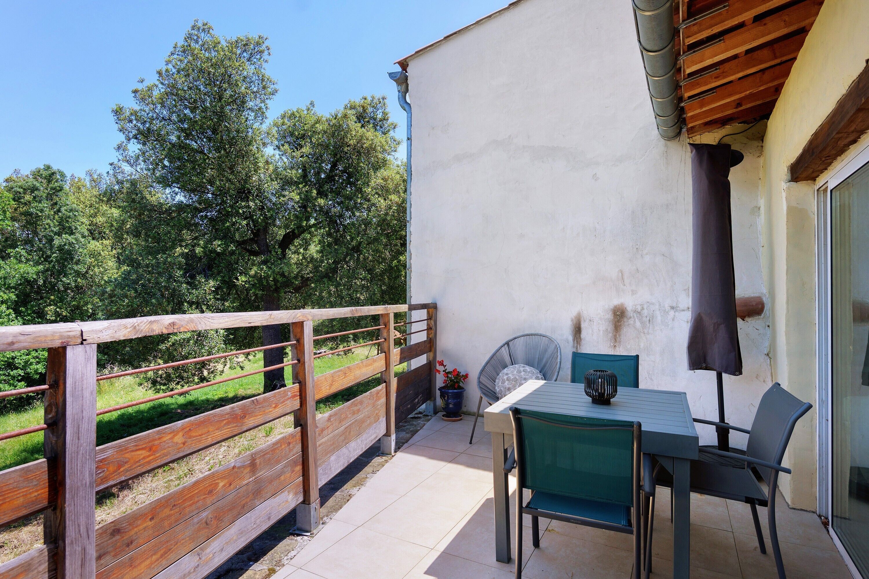 Ein Balkon mit Tisch und Stühlen, einem Holzzaun und Blick auf Bäume.