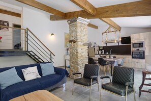 A modern living room with a stone pillar, a blue sofa, and a dining area with chairs and a table.